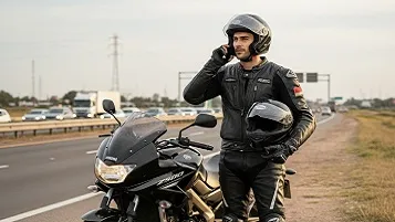 Hombre parado con la moto al lado de la autopista mientras llama por teléfono a una grúa